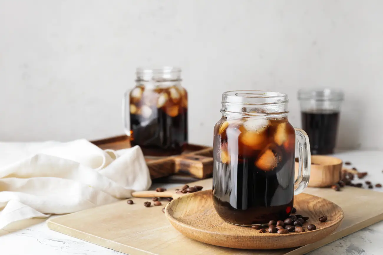 Cold brew z lodem w szklanych słoikach na drewnianej tacy.