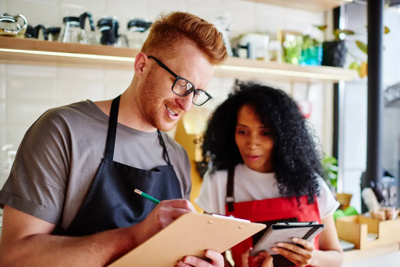 Dwójka pracowników gastronomii analizuje plan na clipboardzie w kuchni.
