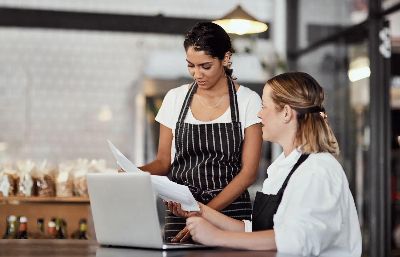 Dwie pracownice gastronomii omawiające dokumenty przy komputerze – analiza danych osobowych i obowiązki zgodne z RODO