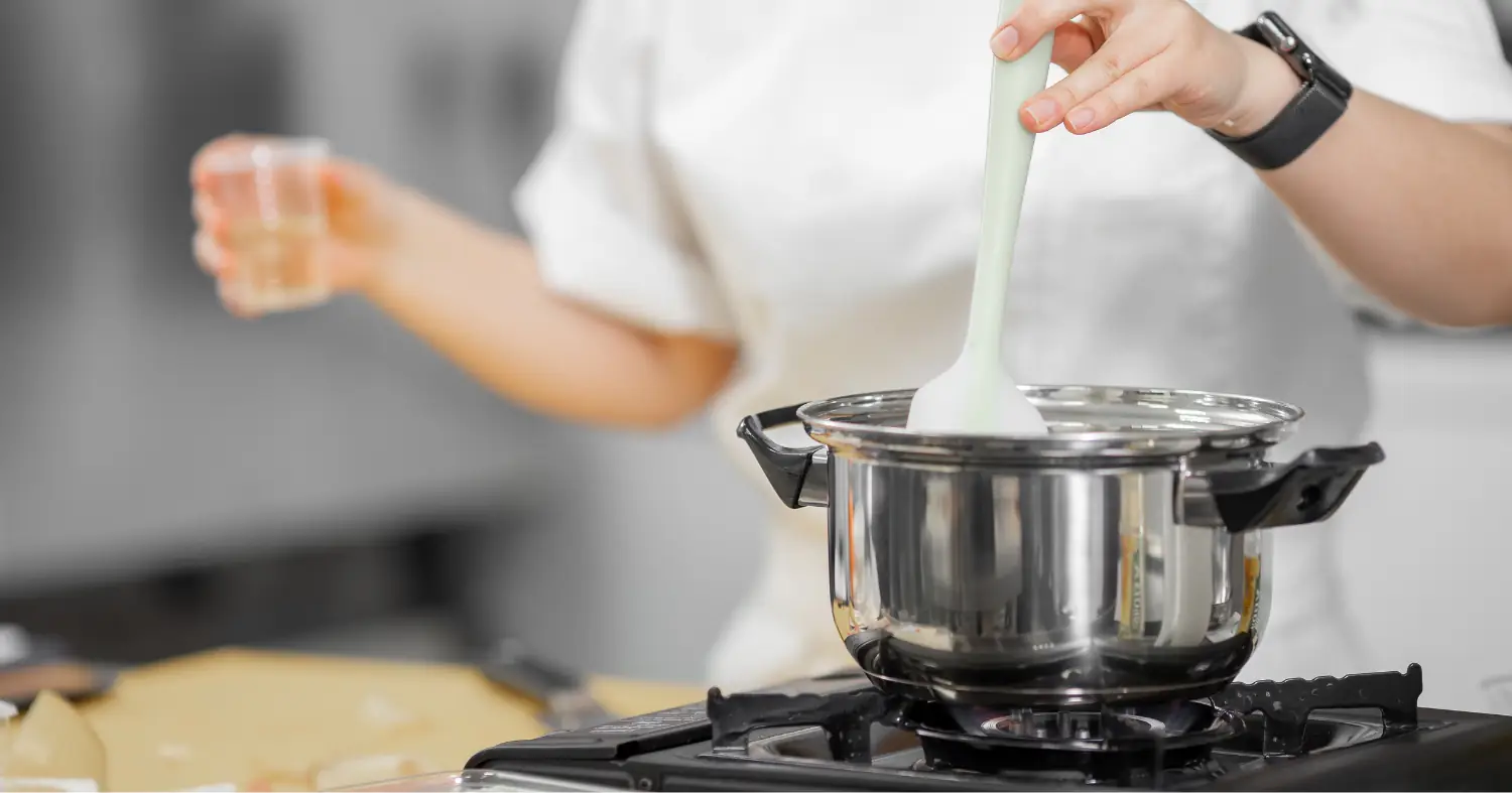 Kucharz miesza składniki w garnku na palniku gazowym