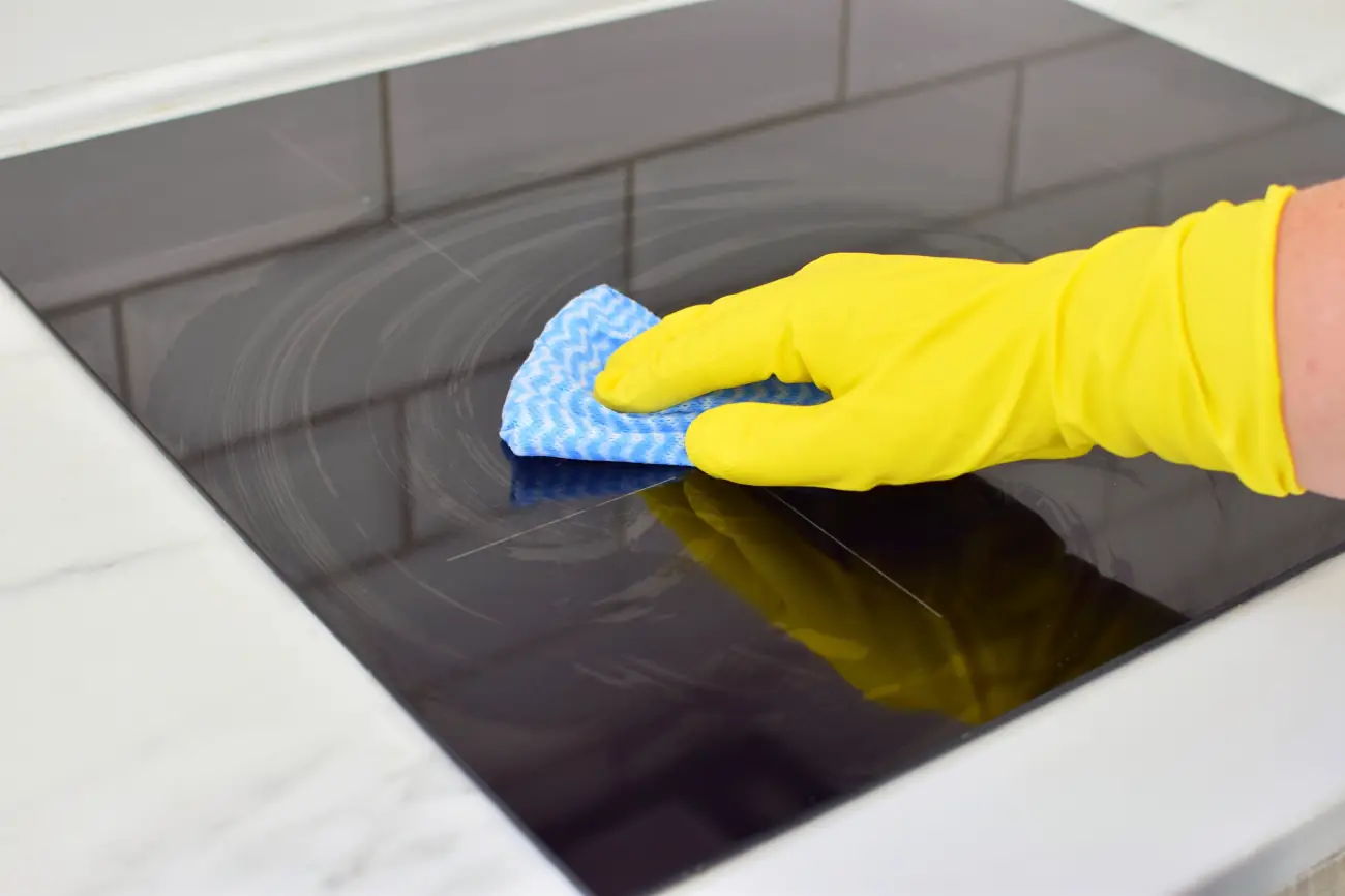 Jak wyczyścić kuchenkę indukcyjną – przecieranie płyty szmatką w gumowej rękawiczce.