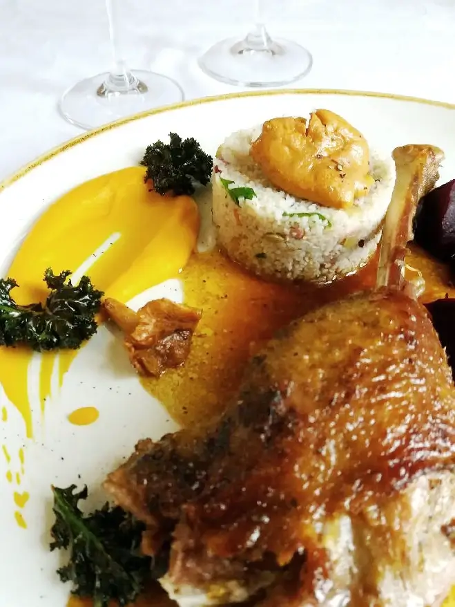Elegancko podane danie z pieczoną gęsiną na Świętego Marcina, serwowaną z musem z dyni, ryżem z warzywami, jarmużem i sosem demi glace, na porcelanowym talerzu z delikatnym złotym rantem.