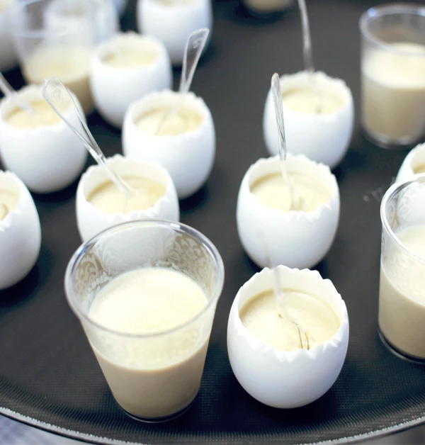 Nietypowa przystawka – panna cotta z tuńczyka, podana w eleganckich, białych miseczkach i przezroczystych kieliszkach, każda porcja z plastikową łyżeczką, ułożone na czarnej tacy.