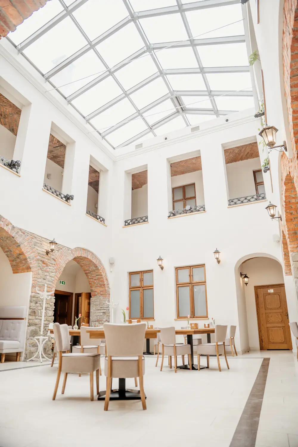 Jasne patio restauracyjne w Kamienicy Konczakowskich z przeszklonym dachem, arkadami z cegły i eleganckimi stołami konsumenckimi.