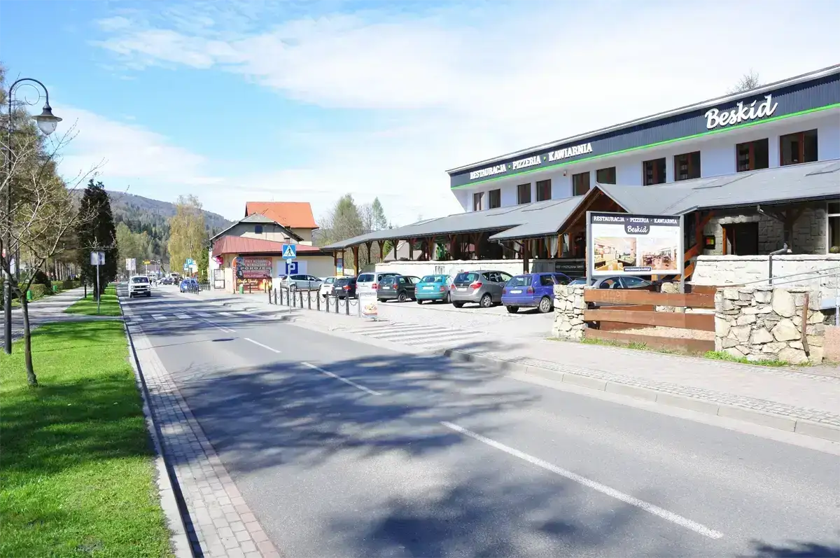 Zewnętrzny widok restauracji Beskid z parkingiem, szyldem i przestronnym tarasem – lokal gastronomiczny w malowniczej górskiej okolicy.