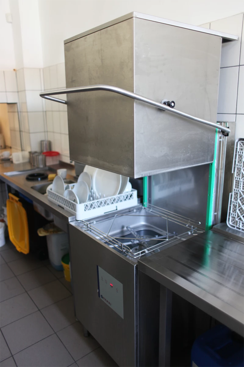 Profesjonalna zmywarka kapturowa z podnoszoną pokrywą w kuchni gastronomicznej.