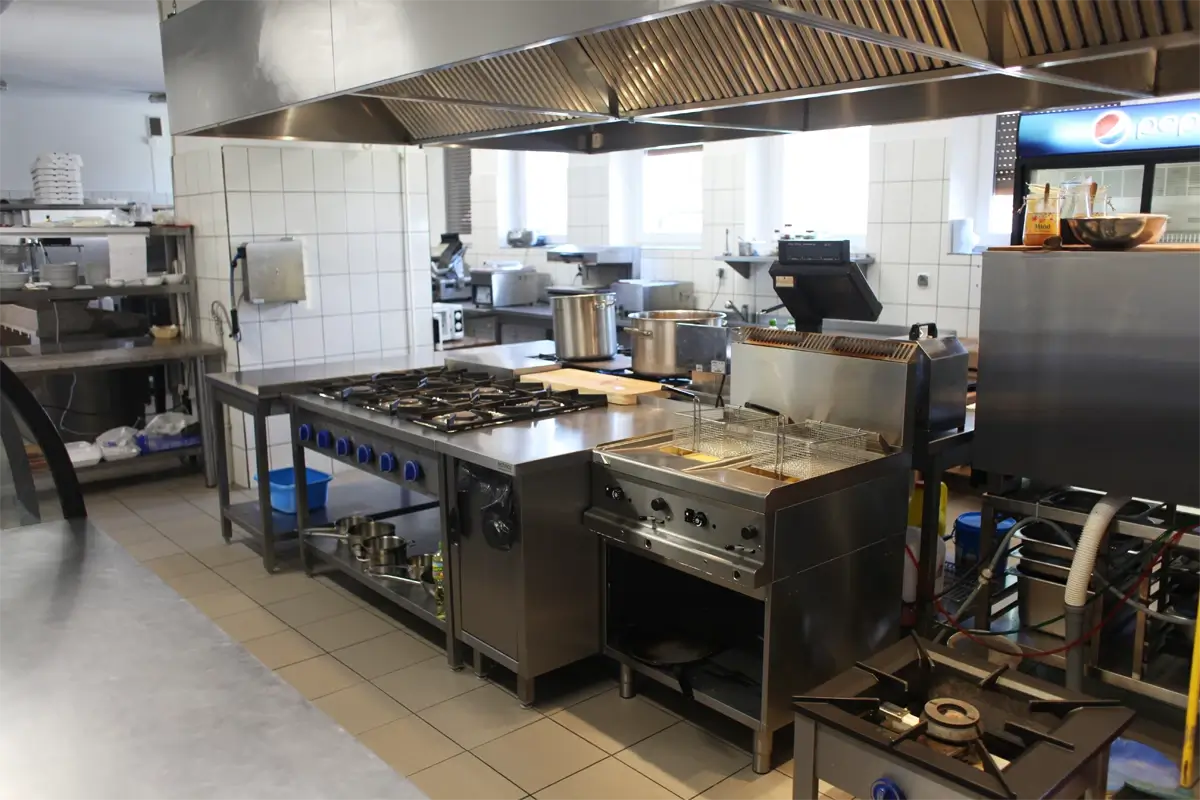 Profesjonalna kuchnia gastronomiczna z kuchnią gazową, frytkownicą, okapem wentylacyjnym i stanowiskami roboczymi.