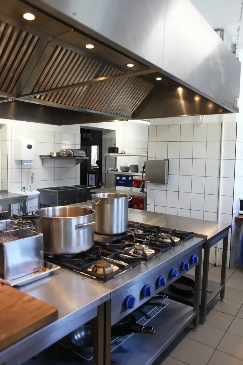 Profesjonalna kuchnia restauracyjna z kuchnią gazową wielopalnikową, frytkownicą i dużym okapem wentylacyjnym.
