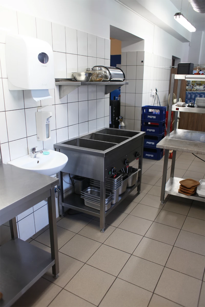 Strefa zmywalni i obróbki w kuchni gastronomicznej z bemarem elektrycznym, umywalką do higieny rąk i stołem roboczym wykonanym ze stali nierdzewnej.