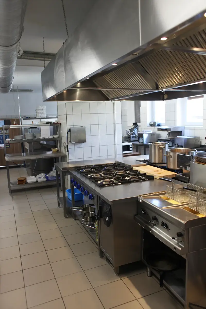 Profesjonalna kuchnia gastronomiczna z centralnym ciągiem grzewczym, kuchnią gazową, frytkownicą i okapem wentylacyjnym.
