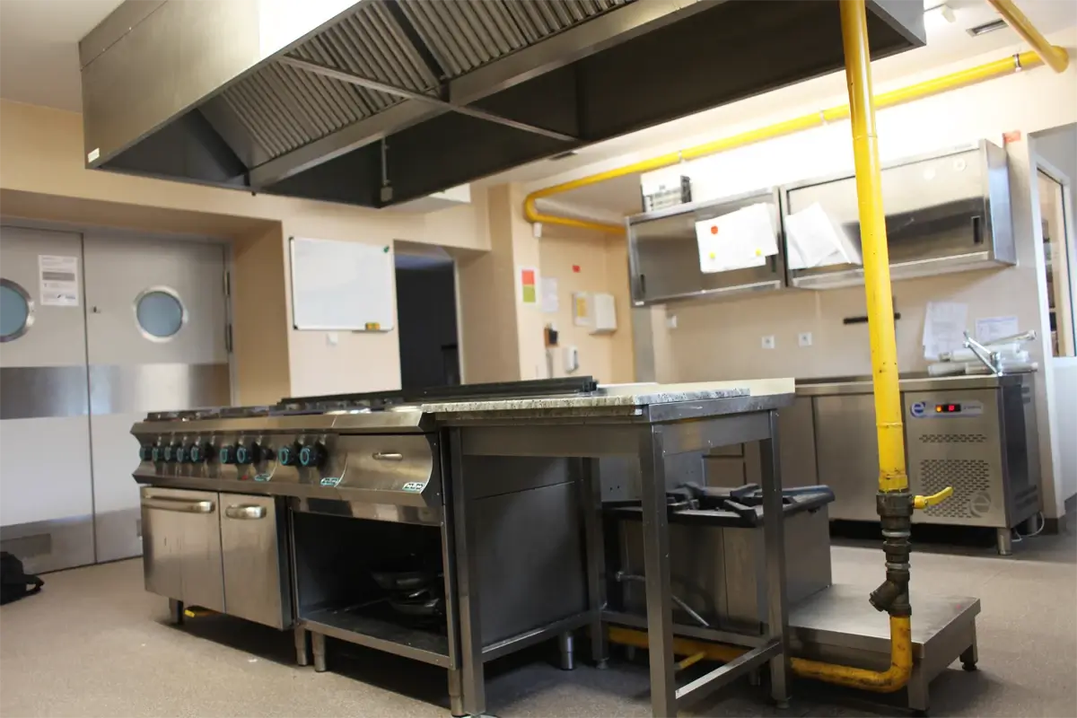 Profesjonalna kuchnia gastronomiczna z kuchnią gazową wielopalnikową, stołem roboczym, okapem wentylacyjnym i instalacją gazową.