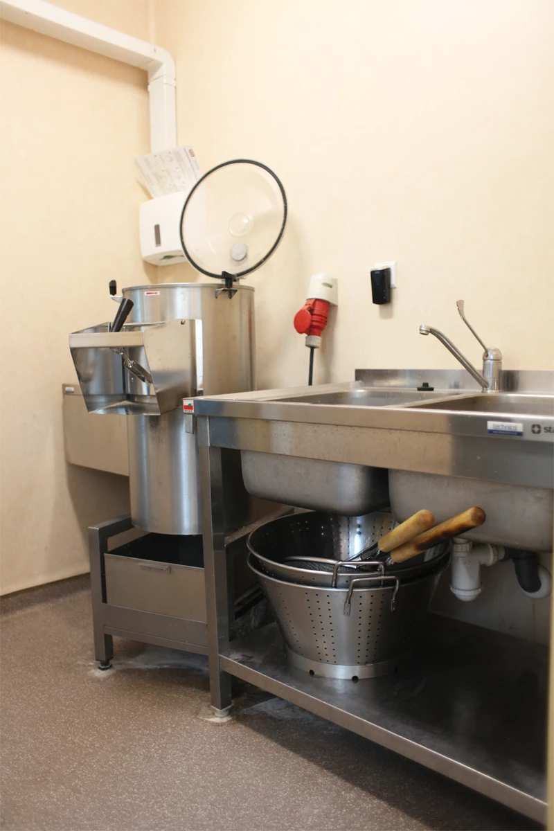 Strefa obróbki wstępnej w kuchni gastronomicznej z obieraczką do warzyw, zlewem dwukomorowym i stołem ze stali nierdzewnej.