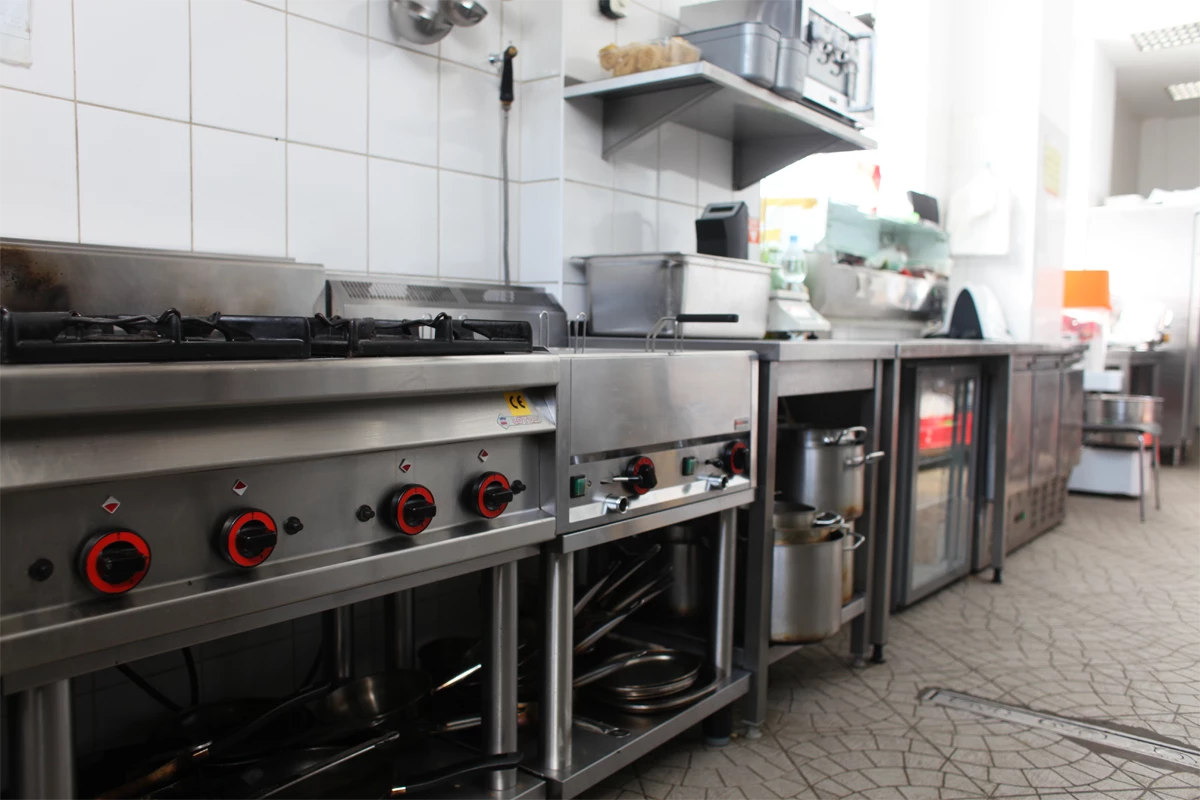 Linia technologiczna w kuchni gastronomicznej – kuchenka gazowa wielopalnikowa, frytownica, pojemniki GN z naczyniami, blat roboczy ze zlewem, chłodziarki podblatowe i urządzenia gastronomiczne.