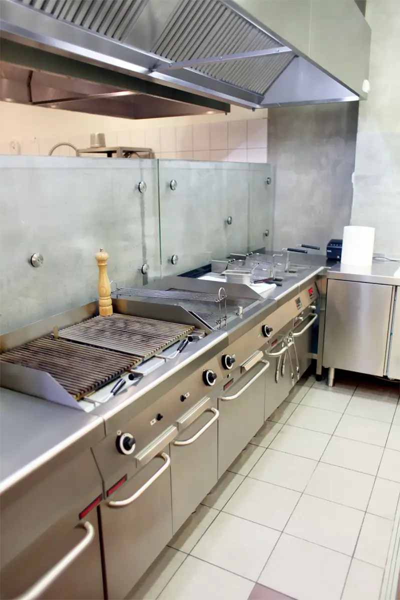 Profesjonalna linia grzewcza w kuchni gastronomicznej – grill kontaktowy, płyta grillowa, frytownica i kuchenka gastronomiczna pod wyciągiem wentylacyjnym ze stali nierdzewnej, przeznaczone do intensywnego użytkowania w restauracjach.