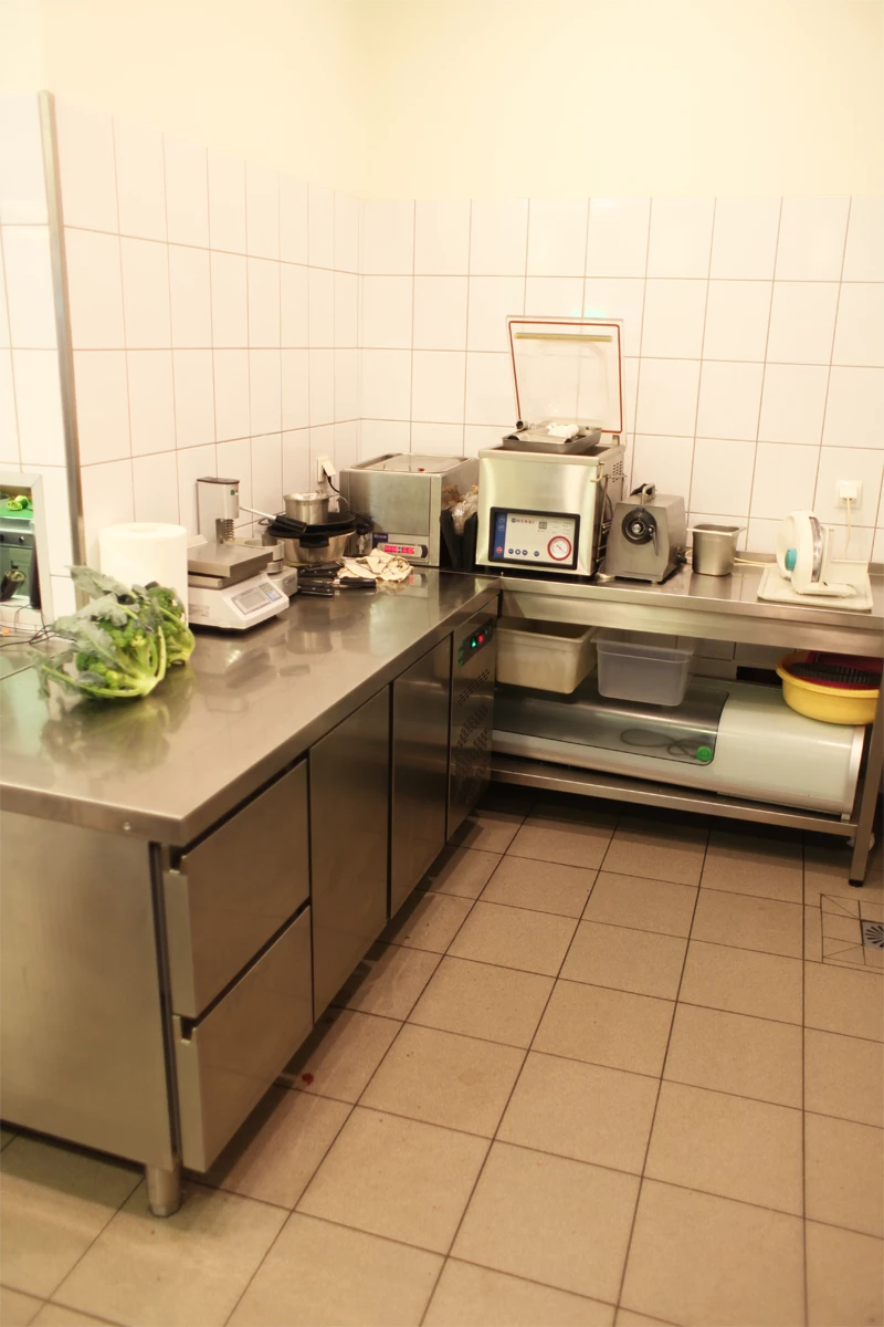 Stanowisko przygotowawcze w kuchni gastronomicznej z urządzeniem do pakowania próżniowego, chłodziarką podblatową i wagą elektroniczną na blacie ze stali nierdzewnej.