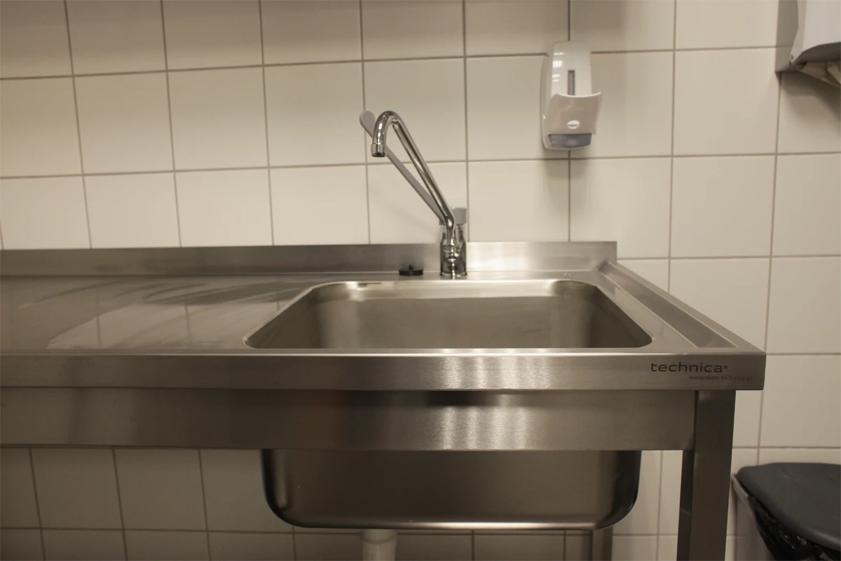 Zbliżenie na zlew z długą baterią, zainstalowaną na roboczym blacie kuchennym. W tle widoczny dozownik na mydło oraz pojemnik na śmieci.