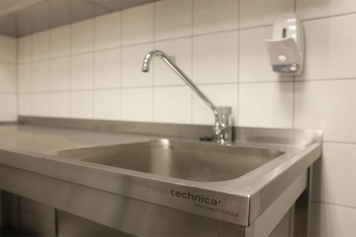 Zlew gastronomiczny ze stali nierdzewnej Technica z nowoczesną baterią, na tle białych płytek ściennych, zaprojektowany do intensywnego użytkowania w profesjonalnej kuchni.