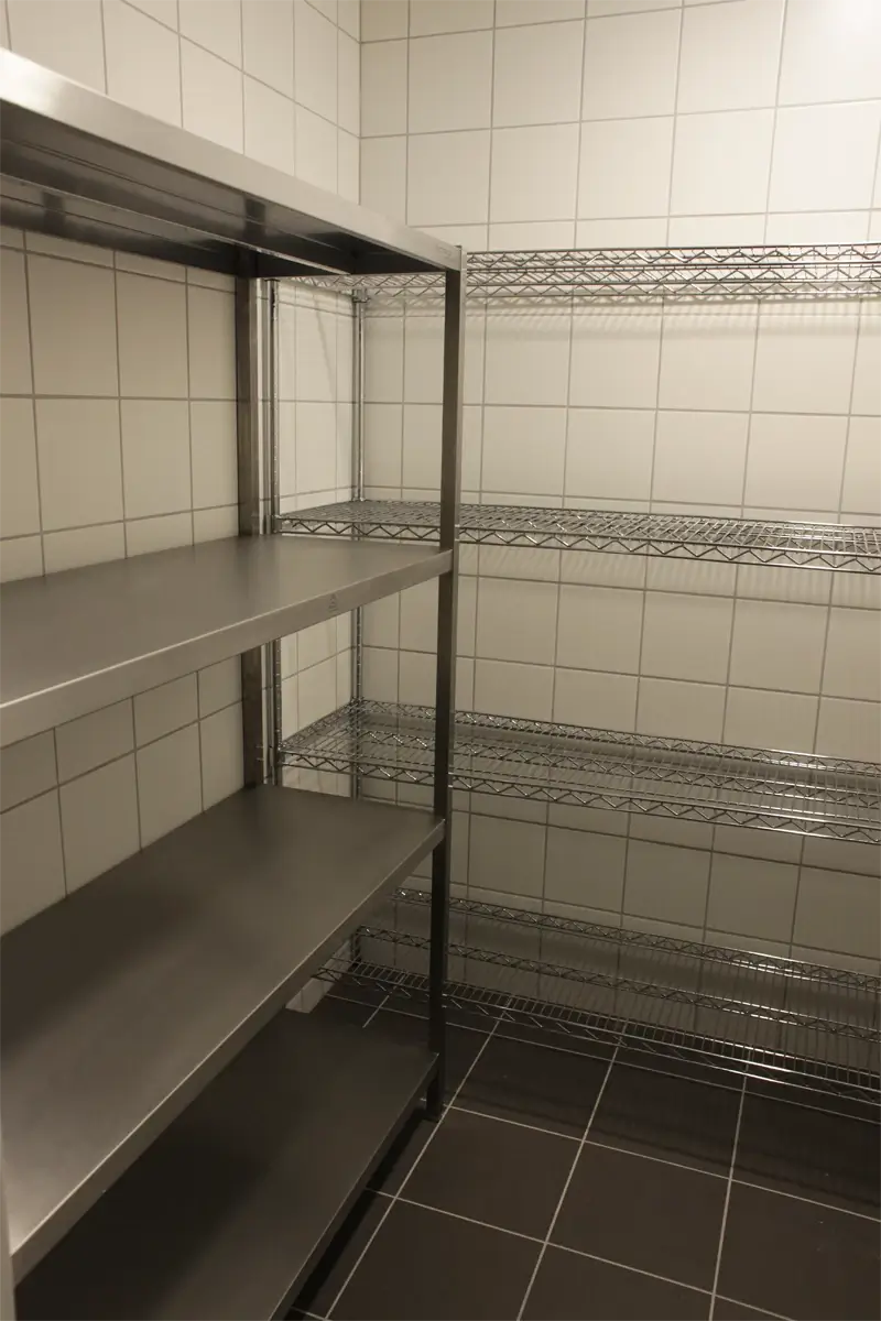 Regały magazynowe przeznaczone do przechowywania produktów i sprzętu w zapleczu kuchni gastronomicznej. Przemyślana organizacja przestrzeni dla efektywnego zarządzania zapasami.