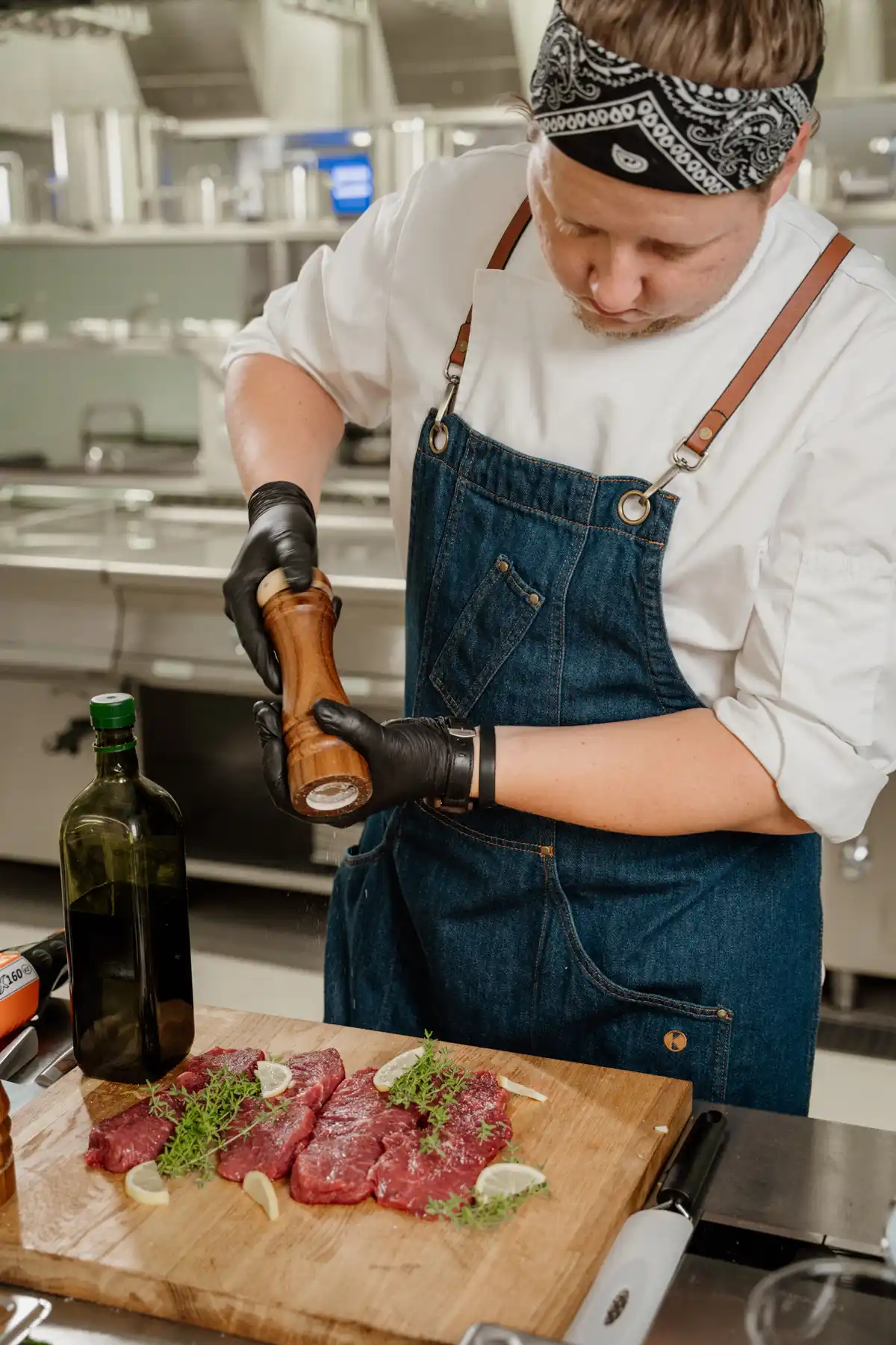 Szef kuchni Tomasz Rymisz doprawia mięso świeżo mielonym pieprzem w profesjonalnej kuchni gastronomicznej.