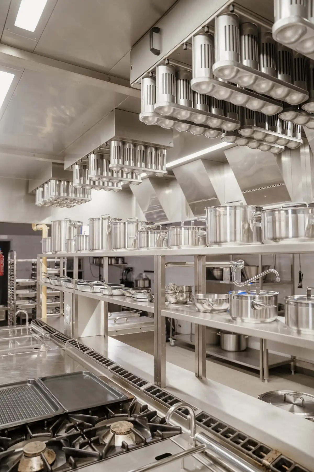 Profesjonalna kuchnia gastronomiczna ze stalowym wyposażeniem, okapami i zestawem garnków.