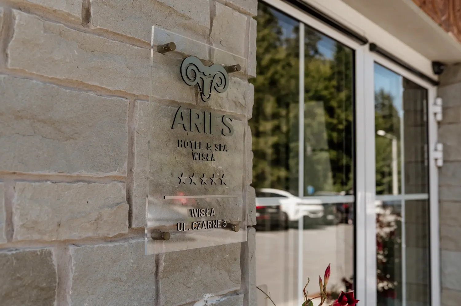 Tablica informacyjna Aries Hotel Spa przy wejściu do hotelu, detal elewacji obiektu hotelowego.