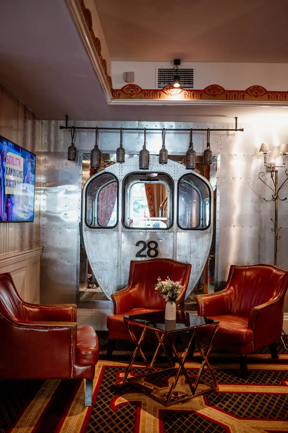 Stylowa strefa lounge w hotelu z fotelami skórzanymi i designerską ścianą inspirowaną motywem kolejowym.