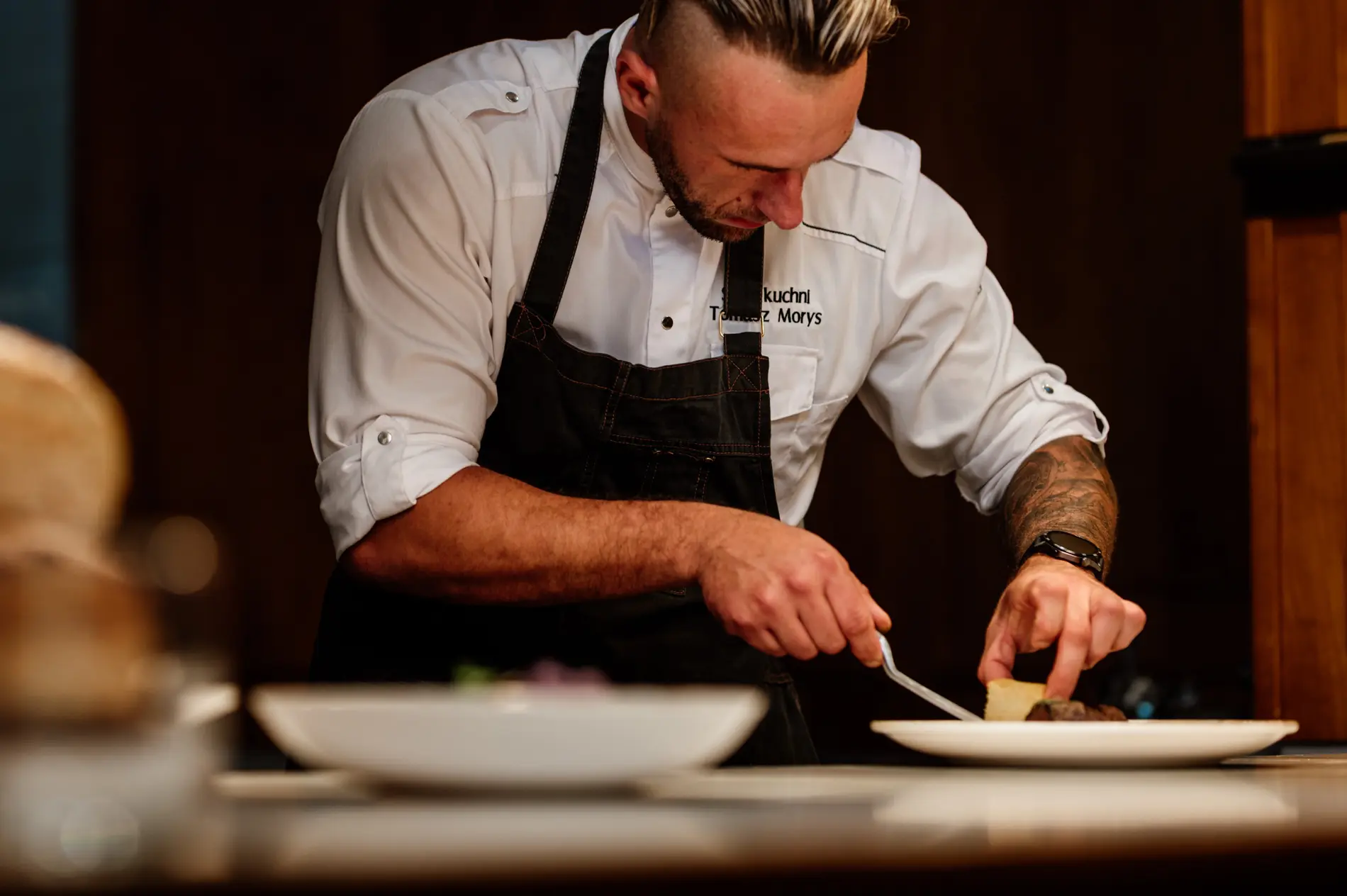 Szef kuchni Tomasz Morys precyzyjnie wykańczający danie podczas serwisu w profesjonalnej kuchni restauracyjnej.
