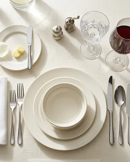 Porcelanowa miska sztaplowana w eleganckim nakryciu stołu restauracyjnego z białym obrusem, sztućcami i kieliszkami.