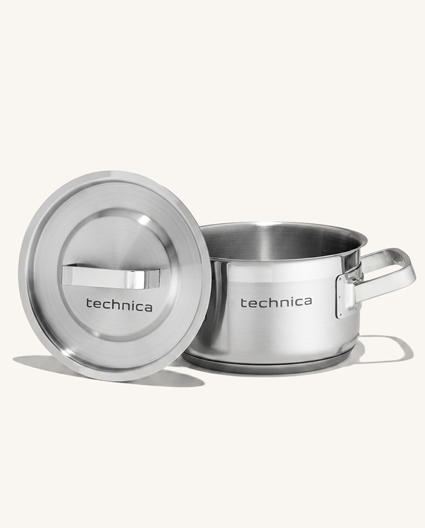 Garnek ze stali nierdzewnej Technica z pokrywką, widok frontalny. Po lewej stronie ustawiona stalowa pokrywka z uchwytem i logo Technica, po prawej garnek z szerokim metalowym uchwytem. Produkt sfotografowany na jasnym, neutralnym tle.