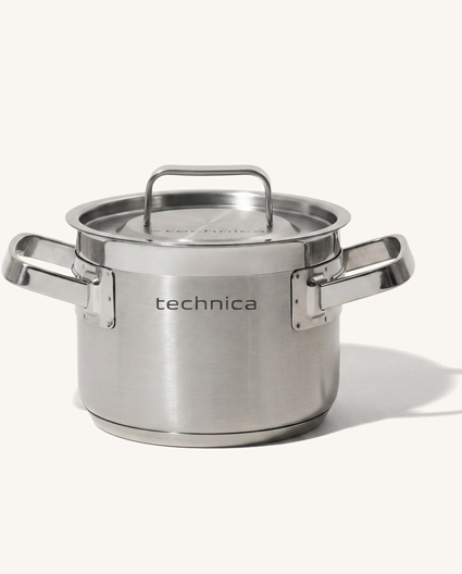 Garnek Technica ze stali nierdzewnej z pokrywką, widok od przodu. Produkt wyposażony jest w dwa szerokie metalowe uchwyty oraz stalową pokrywę z centralnym uchwytem. Na froncie korpusu widoczne logo Technica. Garnek sfotografowany na jasnym, neutralnym tle.
