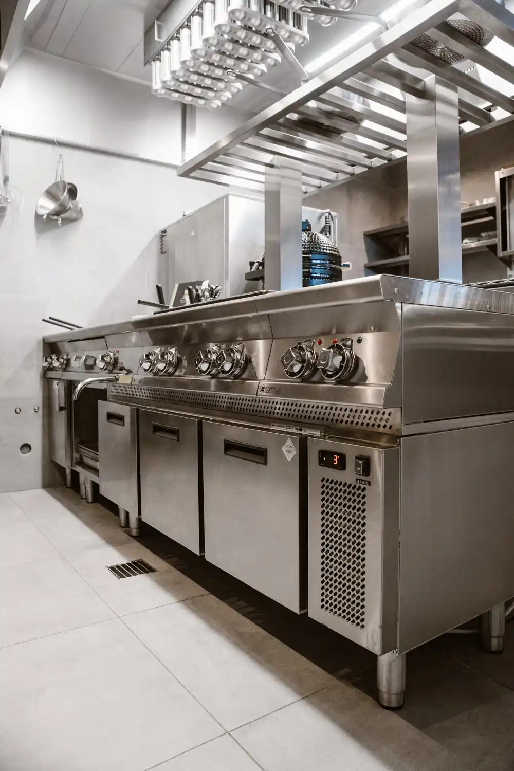 Profesjonalna linia grzewcza ze stali nierdzewnej w restauracyjnej kuchni – grill, płyta grzewcza i chłodzone szafki podblatowe w zapleczu gastronomicznym.